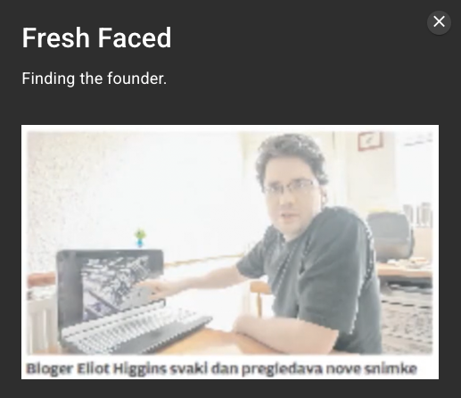 A photo of Eliot Higgins, founder of Bellingcat, sitting at a desk with a laptop open. The image is captioned in a foreign language.